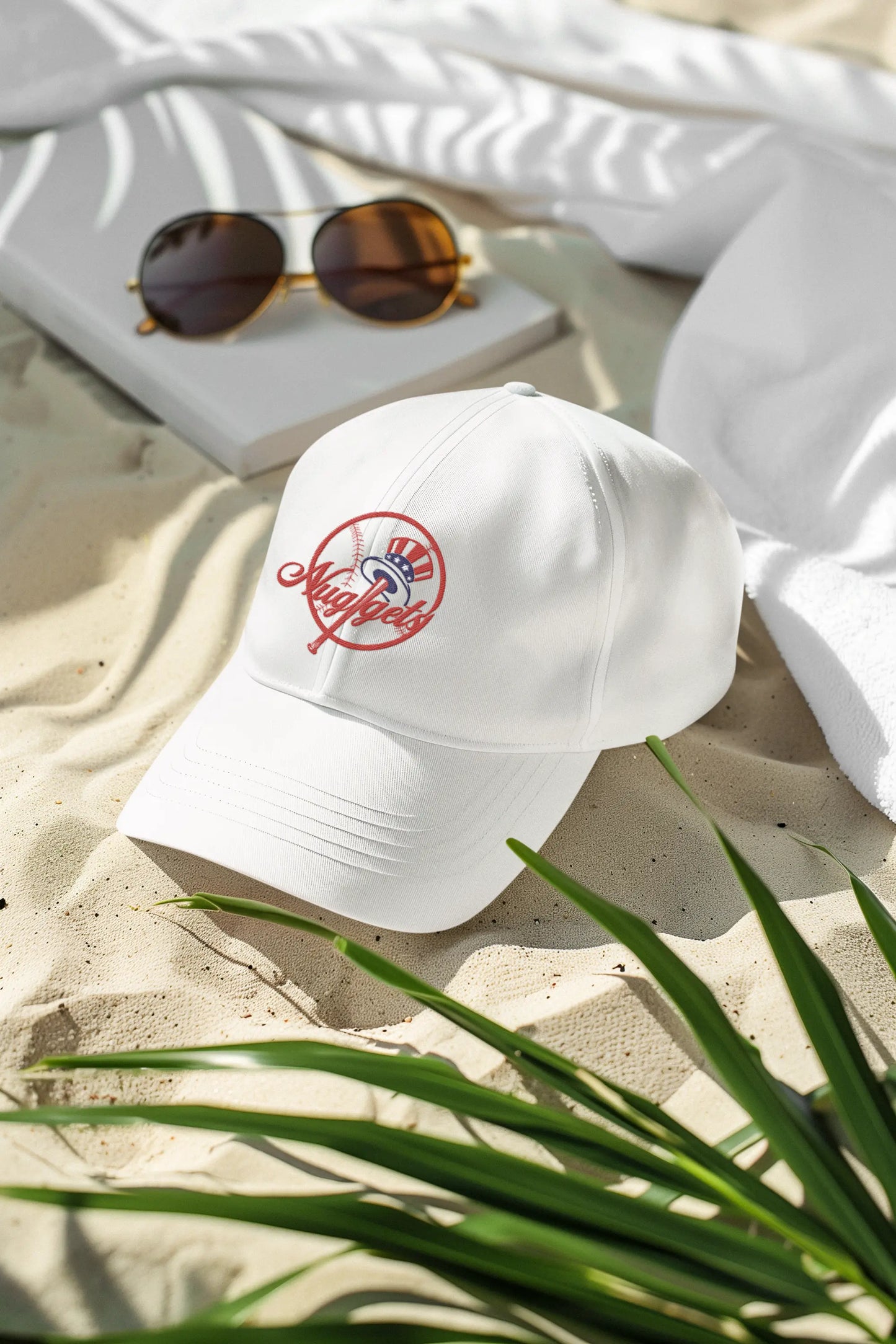 White New York Nuggets dad hat with red embroidered logo placed on sand beside sunglasses and book.