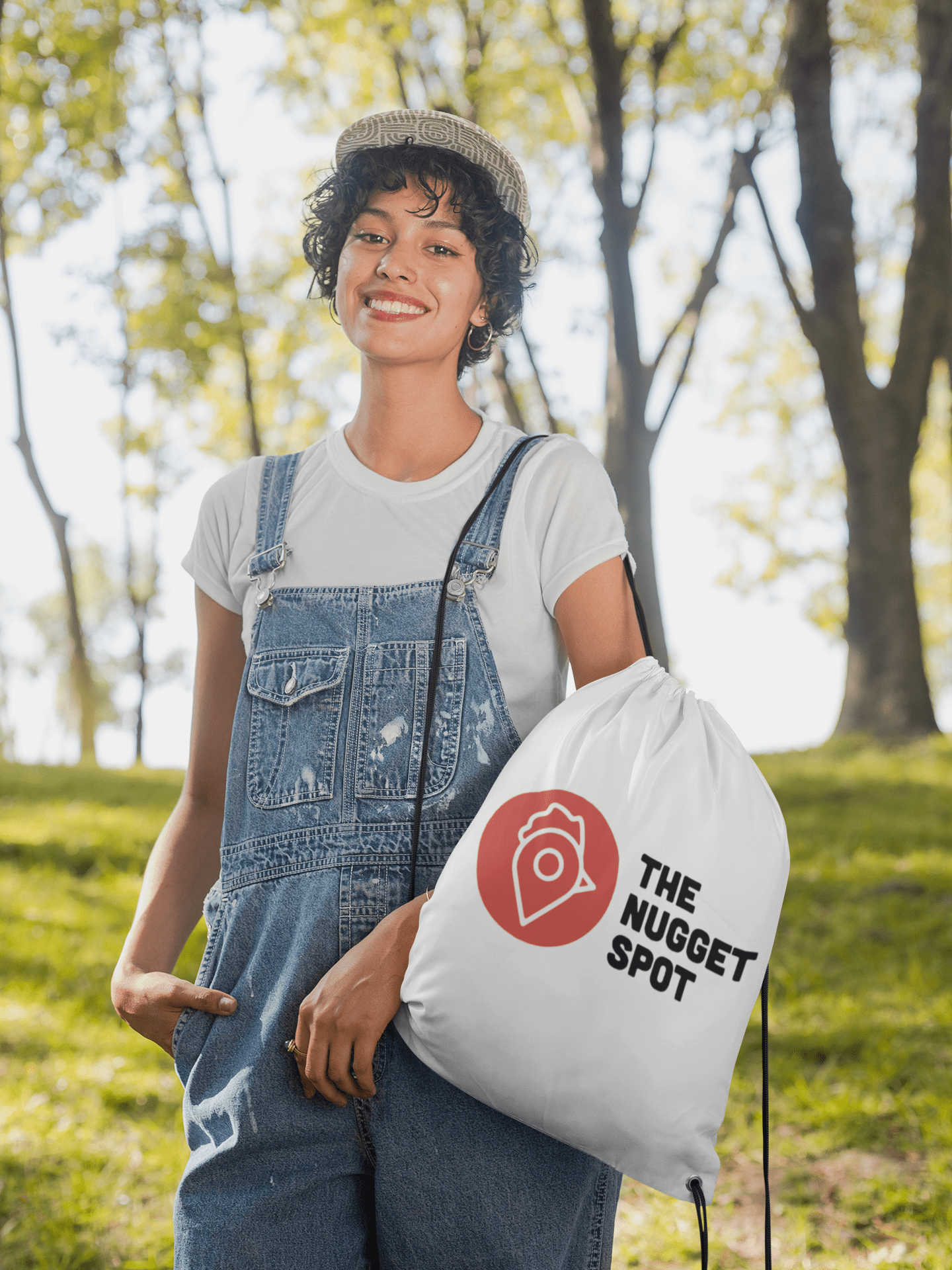 Woman outdoors wearing The Nugget Spot Drawstring Bag over denim overalls