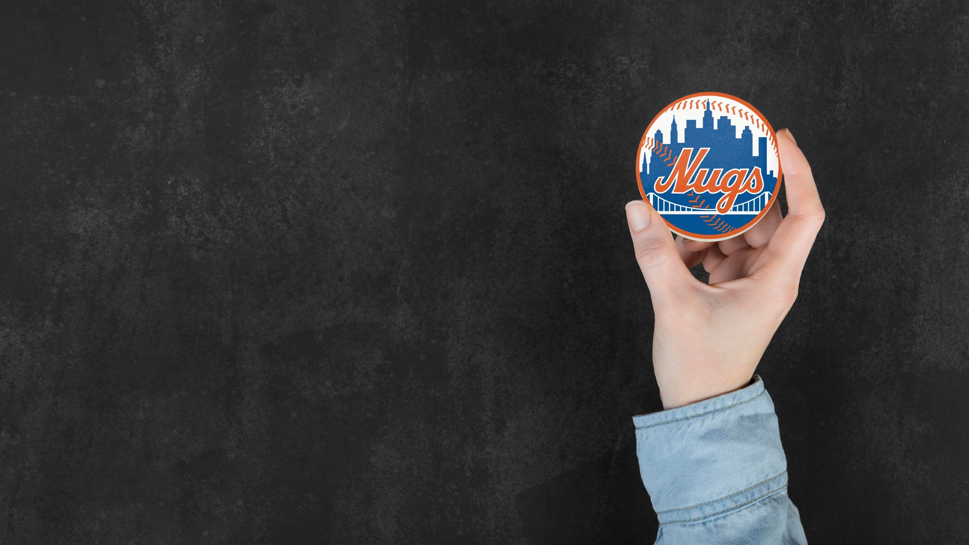 Hand holding the New York Nugs circular vinyl sticker with skyline and baseball-inspired design against dark background.