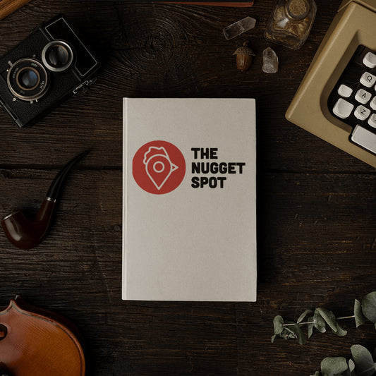 The Nugget Spot hardcover notebook on a rustic wooden desk beside vintage camera and violin.