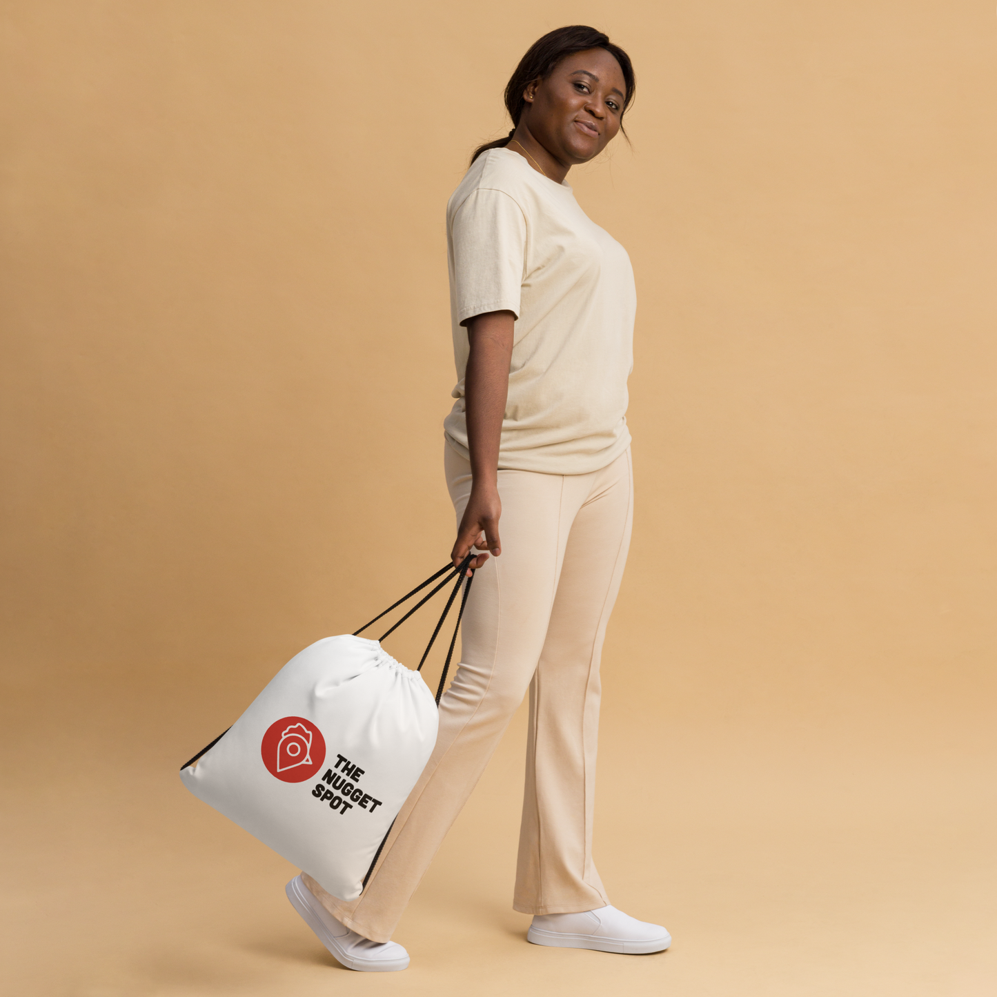 Woman posing against beige background holding The Nugget Spot Drawstring Bag
