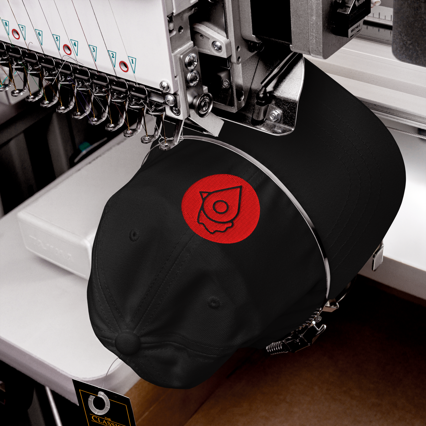 Black dad hat with The Nugget Spot red logo being embroidered on a machine.