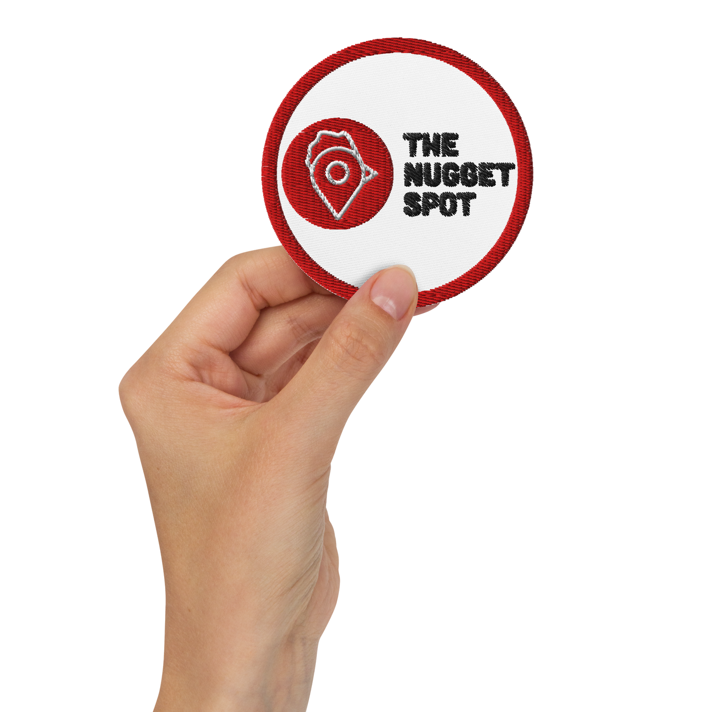 Hand holding The Nugget Spot embroidered patch – premium 3-inch circular patch with crisp stitching and red border.
