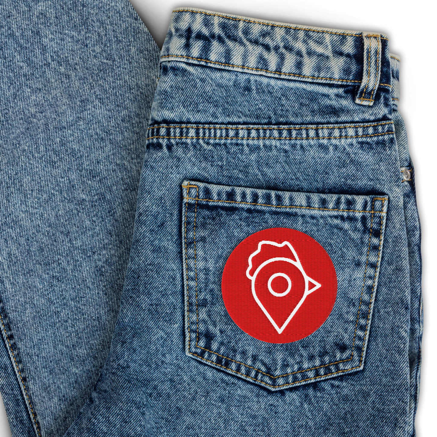 Red circular embroidered patch with white Nugget Spot logo on denim jeans pocket.