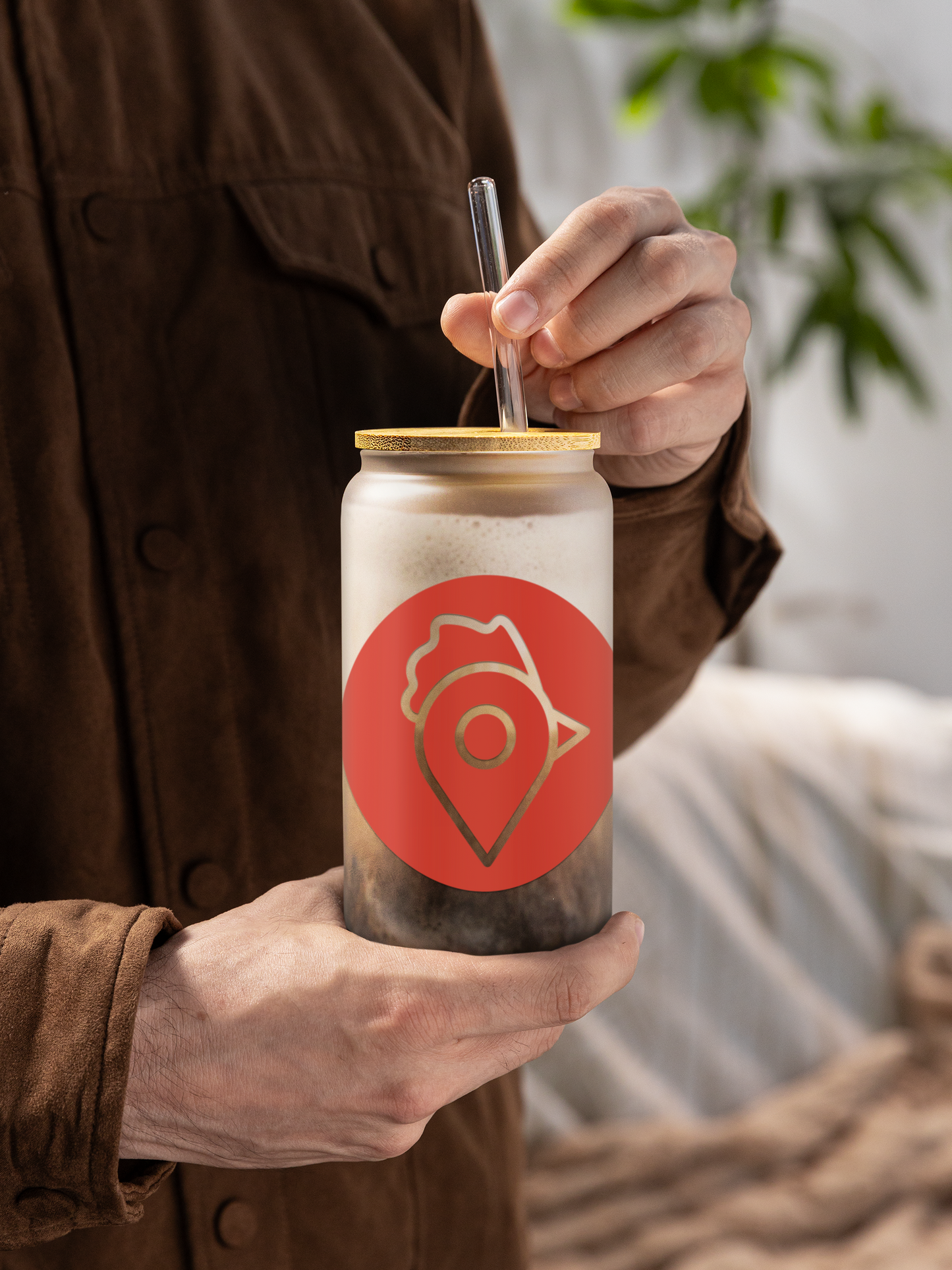 A man in a brown jacket holding The Nugget Spot can-shaped glass with iced coffee and bamboo lid.
