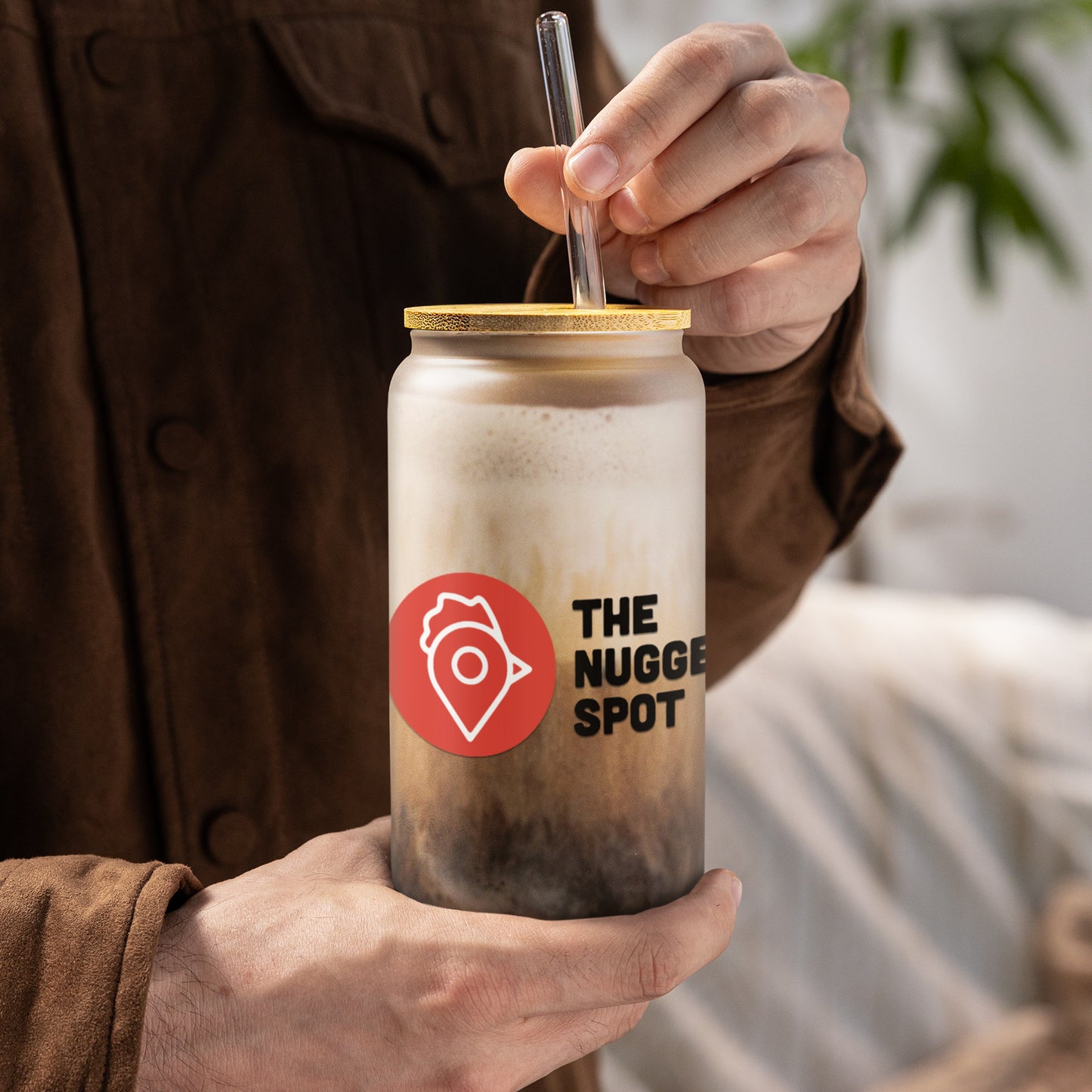 Person holding The Nugget Spot 16oz can-shaped glass with iced coffee and bamboo lid