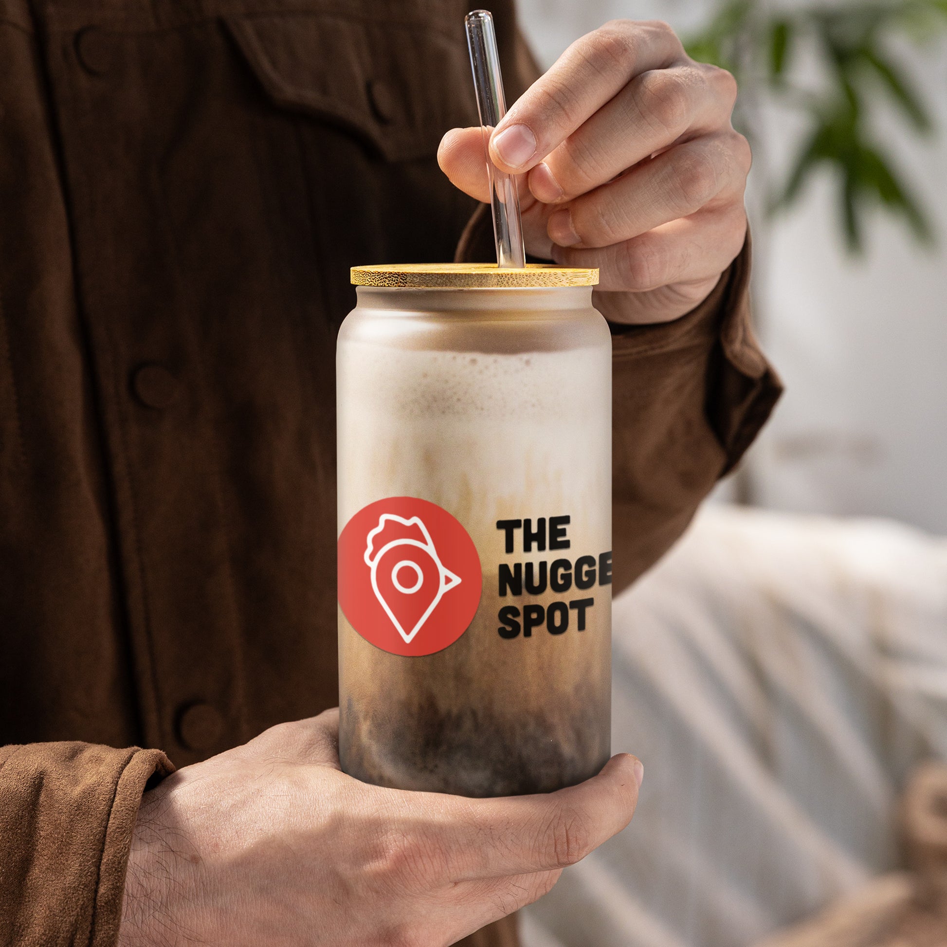 Person holding The Nugget Spot 16oz can-shaped glass with iced coffee and bamboo lid