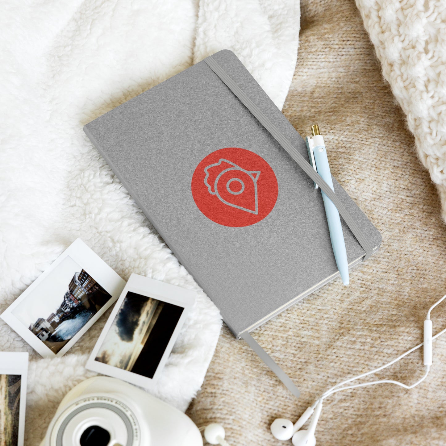 The Nugget Spot grey hardcover notebook resting on a cozy blanket beside photos, pen, and earphones