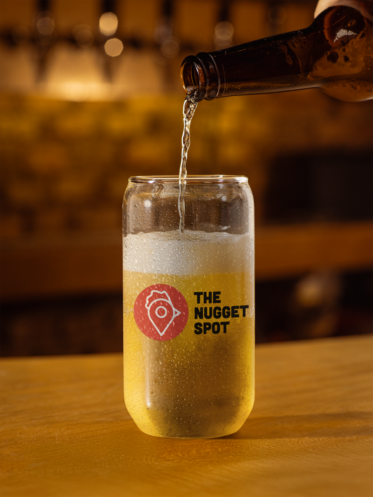 Beer being poured into The Nugget Spot can-shaped glass on wooden counter
