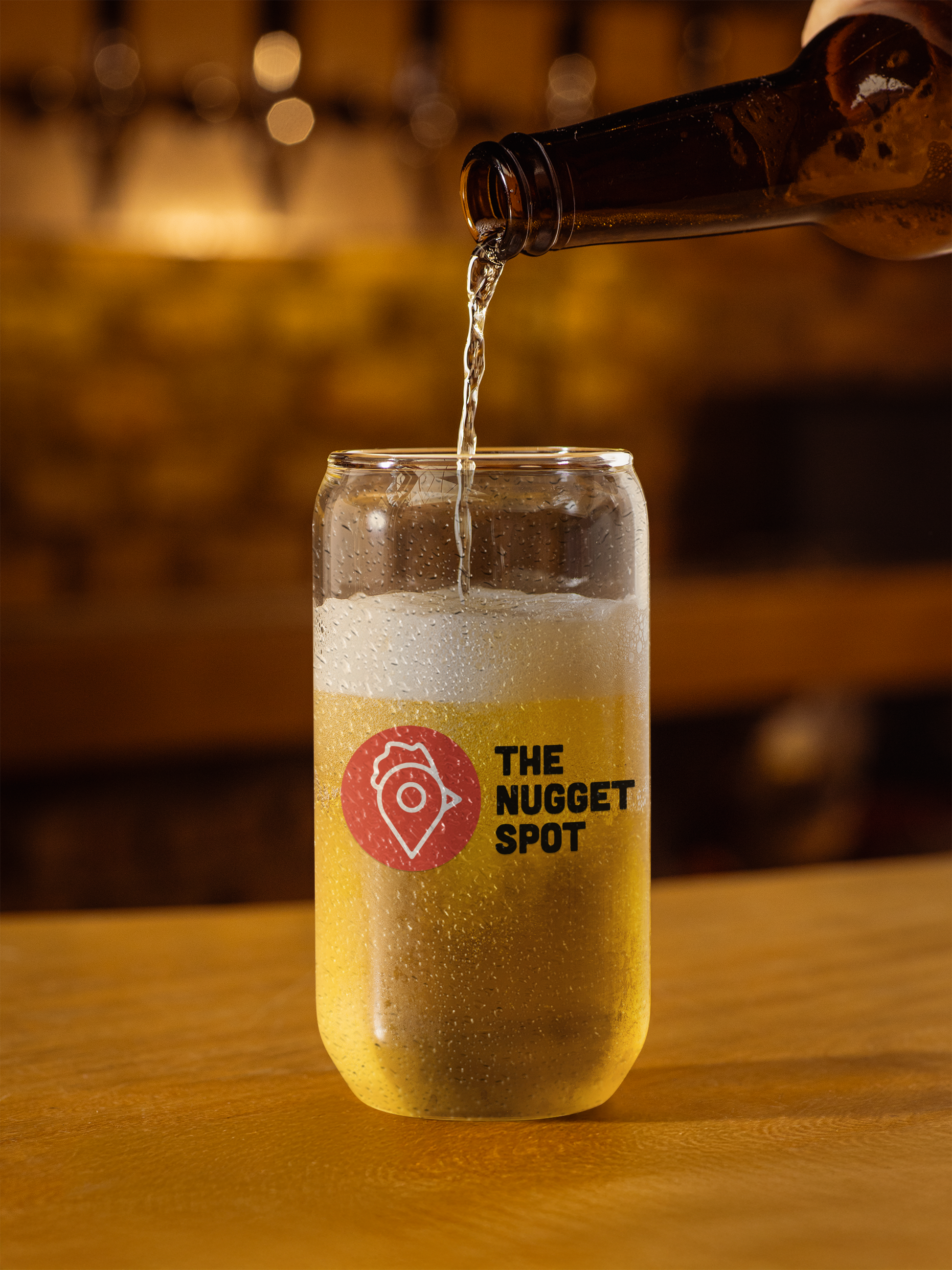 Beer being poured into The Nugget Spot can-shaped glass on wooden counter
