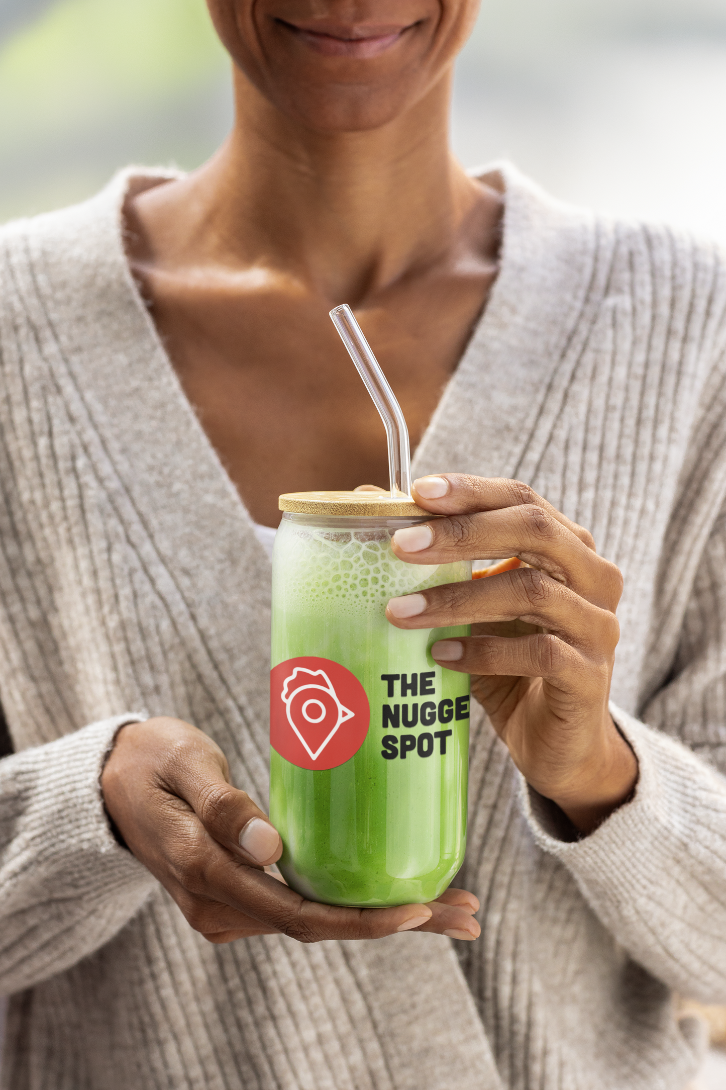 Woman holding The Nugget Spot can-shaped glass with green smoothie and bamboo lid