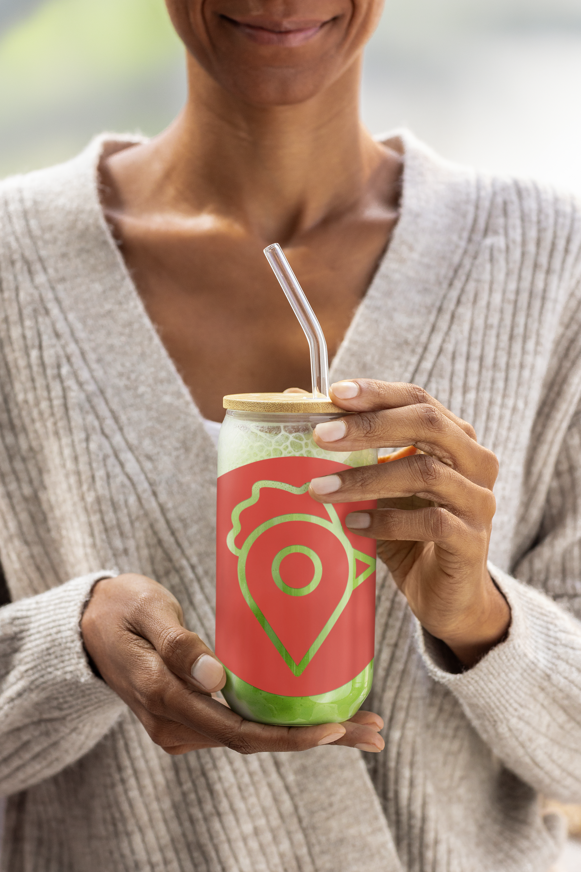 A woman holding The Nugget Spot can-shaped glass with bamboo lid and glass straw, filled with green smoothie.