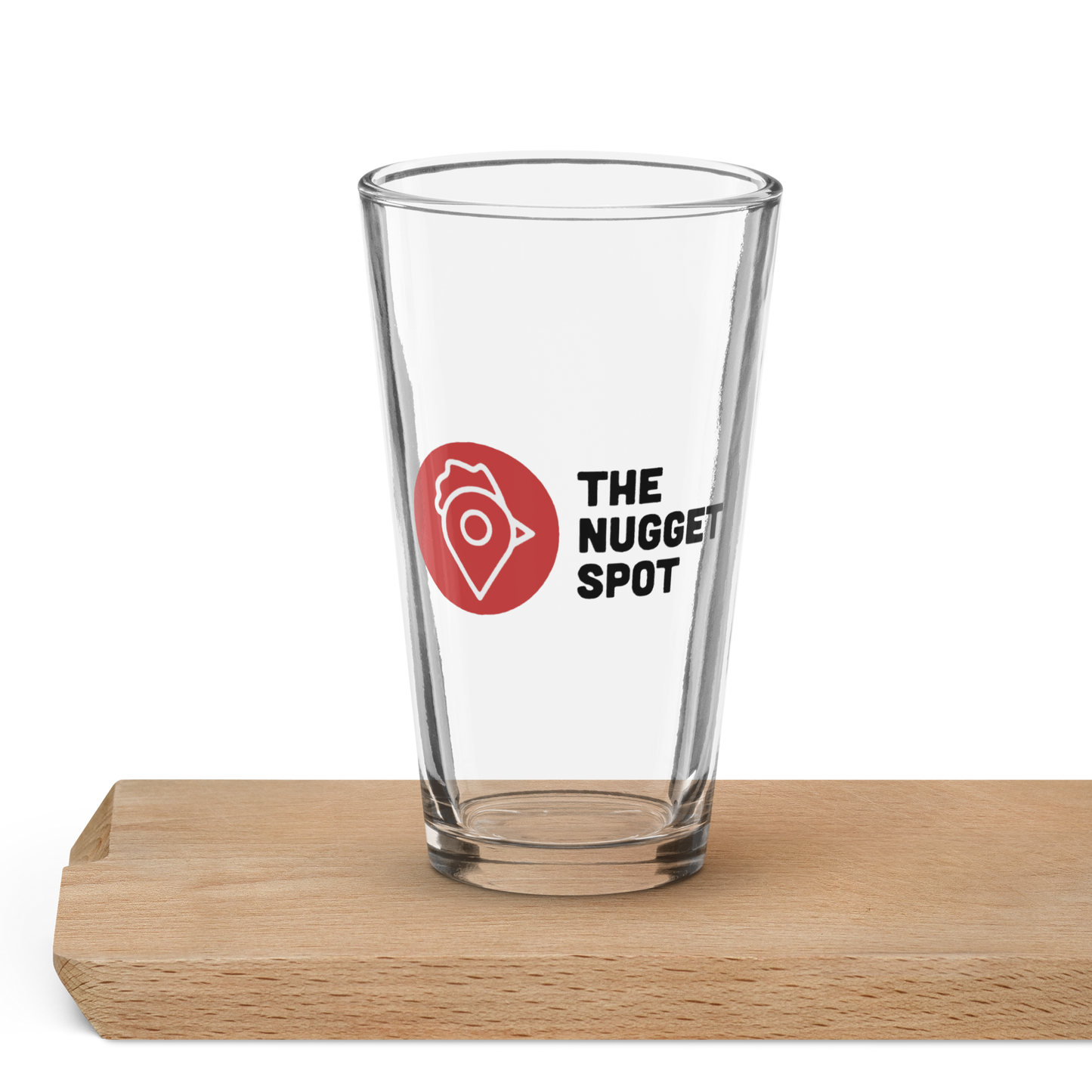 The Nugget Spot 16oz Pint Glass displayed on wooden surface – premium clear glass for beer, cocktails, or daily drinks.