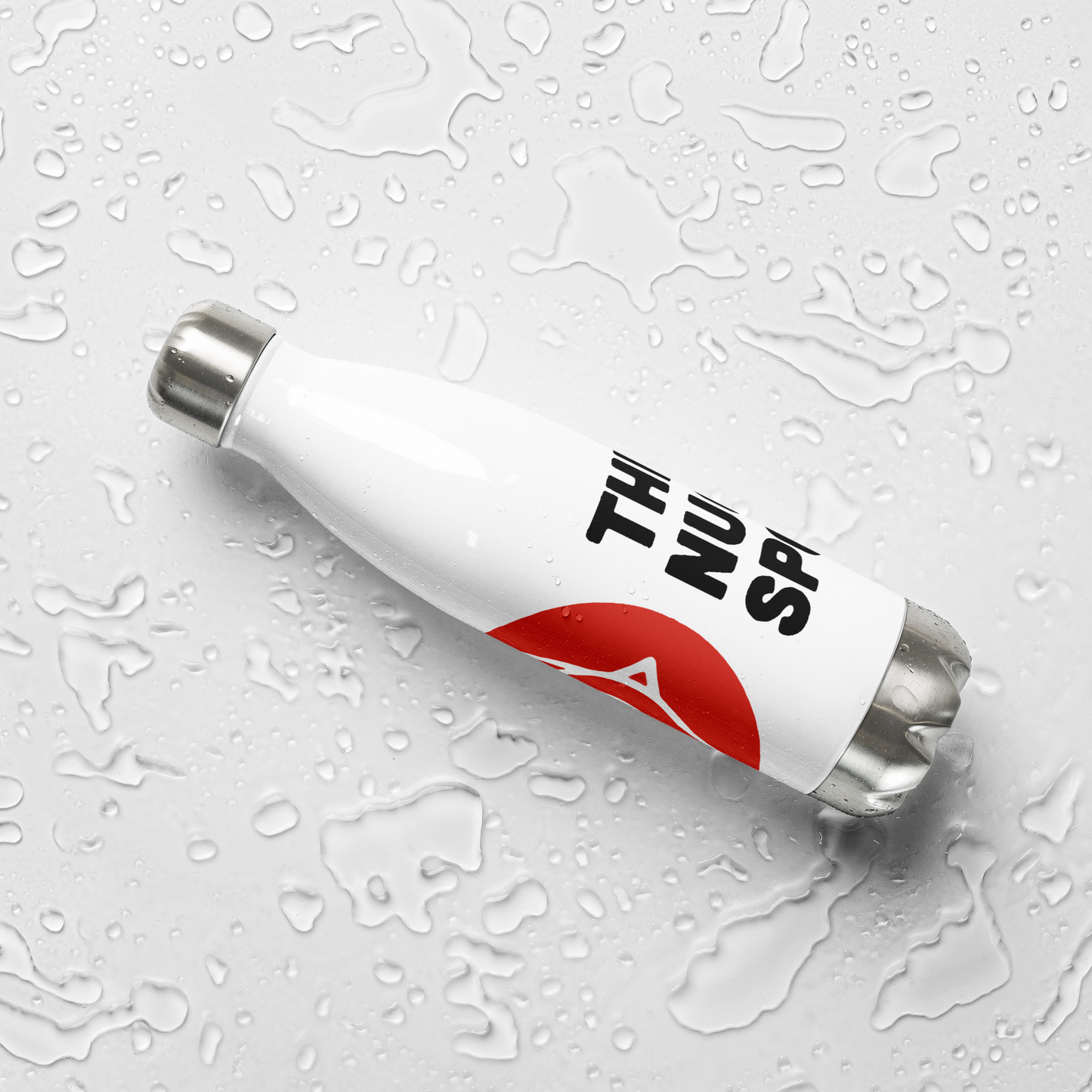 The Nugget Spot 17oz Stainless Steel Water Bottle placed flat on a wet white surface with water droplets.